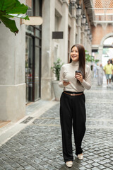 Fototapeta premium Pretty woman holding coffee cup and phone while walking or looking around in shopping mall or market