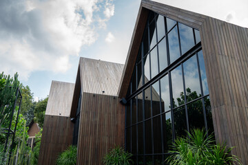 barn house architecture with wooden facade and large glass windows under a cloudy sky. This contemporary exterior design with tropical garden is ideal for real estate and luxury living © Yellow Boat