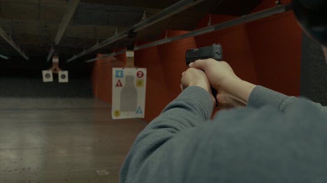 POV of person actively shooting handgun at paper targets inside an indoor shooting range. Controlled firearm use, marksmanship training, safe target practice.