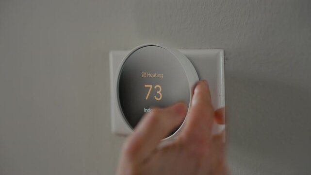 Close-up of a hand adjusting a smart home thermostat showing a temperature of 73 degrees. energy control, modern home technology, and climate comfort management.