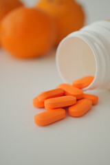 Orange tablets spill from bottle near oranges on table