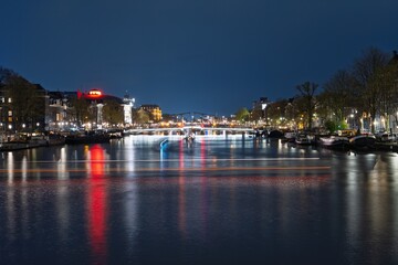 Discover the charm of Amsterdam at night with stunning reflections of city lights on the serene...