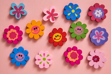 A flat-lay of colourful flower-shaped decorations with cheerful smiley faces on a soft pink background, creating a playful and joyful atmosphere. For Valentine's day or birthday greeting cards