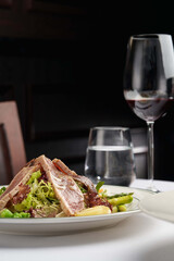 Seared tuna salad with fresh greens, asparagus, and potatoes served in a luxury restaurant with red wine.
