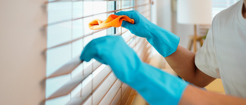 young man worker wear blue glove , cleaning interior work in house, holding wipe, rag cloth dust to clean window blinds. Cleaner and chore service concept