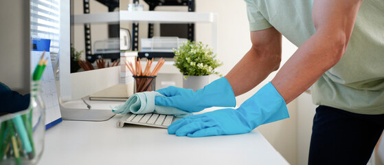 Person cleaning room, cleaning worker is using cloth to wipe computer keyboard in company office room. Cleaning staff. Concept of cleanliness in the organization