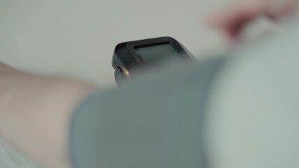 Person sit at table and puts on blood pressure cuff to measure blood pressure using digital monitor. Home healthcare, hypertension awareness, cardiovascular health monitoring.