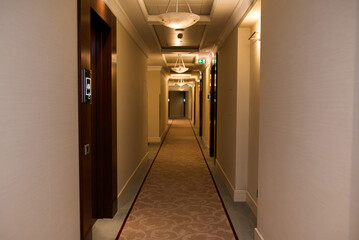 Elegant luxury hotel corridor with warm lighting, carpeted floor, modern wall sconces and refined interior design creating a calm, upscale hospitality atmosphere.
