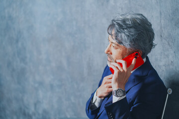 赤いスマートフォンで通話する50代のエグゼクティブ男性