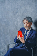 赤いスマートフォンを操作する50代のエグゼクティブ男性