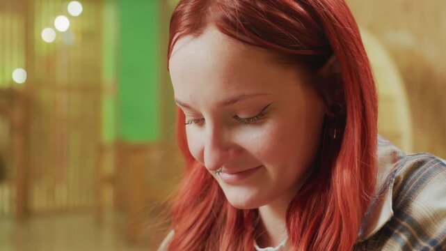 redhead white woman smiling in warm studio looking up with soft grin among string lights and wooden arches, checking notes with satisfied expression, cozy plaid shirt, hopeful entrepreneur moment
