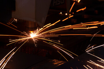 Cutting metal with a laser machine, the laser head cuts the metal, sparks fly when it comes into contact with the surface