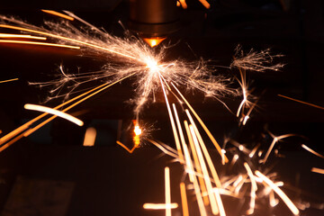 Cutting metal with a laser machine, the laser head cuts the metal, sparks fly when it comes into contact with the surface