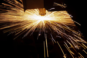 Cutting metal with a laser machine, the laser head cuts the metal, sparks fly when it comes into contact with the surface