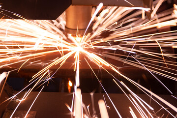 Cutting metal with a laser machine, the laser head cuts the metal, sparks fly when it comes into...