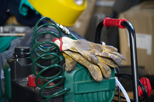 Work gloves resting on an air compressor with a coiled hose and yellow safety helmet