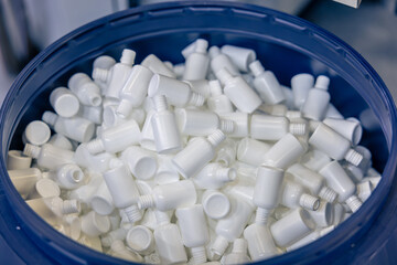 Numerous small white plastic bottles with screw-on necks stacked together. The bottles are empty for cosmetic or pharmaceutical use. Packaging manufacturing