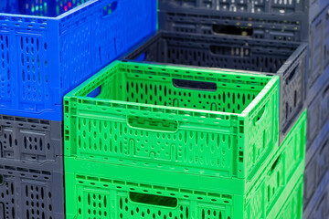 Bright green, blue, and gray stackable plastic crates with ventilation holes on a blurred indoor background, representing storage efficiency