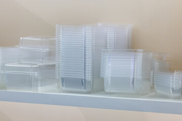 Transparent disposable plastic food containers stacked neatly on a white shelf, photographed in natural light, concept of packaging and storage