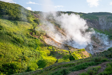 Geothermal landscape with steam and fumaroles in the Valley of Geysers, Kamchatka. Steam rises from the gentle slope of the volcano
