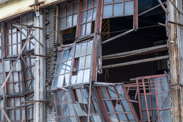 Exterior of old abandoned factory with shattered windows, weathered brick wall, and rusty beams, showing concept of urban decay and neglect