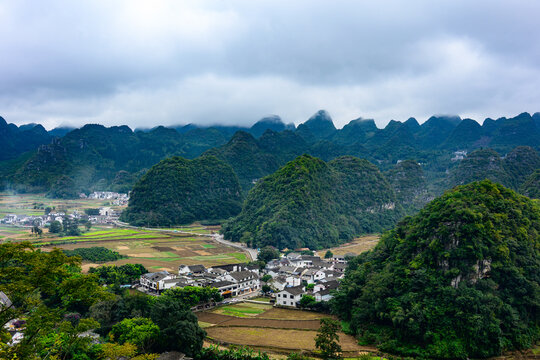 A traditional Buyi village nestled beneath the karst peaks of Wanfenglin, with stone dwellings and terraced fields blending into the majestic Guizhou landscape.
