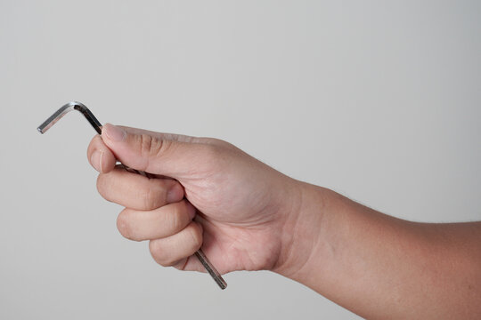 Male person hand holding hexagonal allen L key wrench, over grey