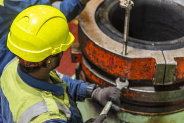 Back view of marine engineer performing maintenance inspection on main engine exhaust valve in ship engine room, industrial maritime environment.