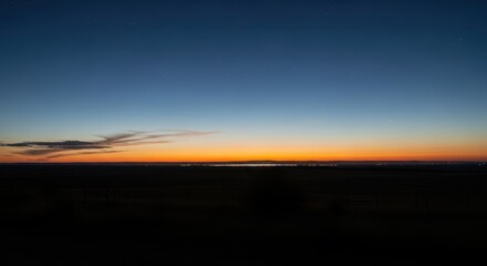 Horizon glows intensely orange above dark landscape under a deep blue twilight sky
