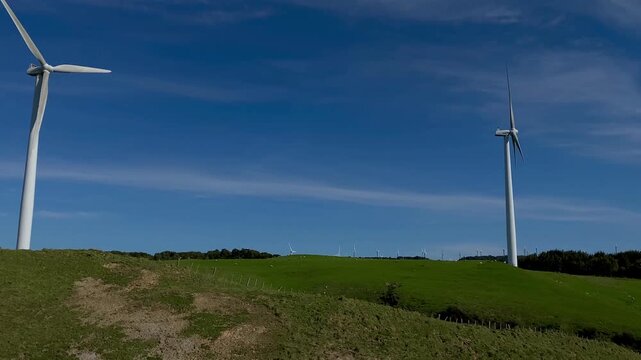 arge wind turbines on rolling green hills under a bright blue sky