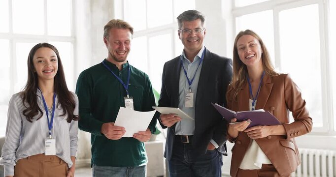 Portrait of happy business team, workshop attendees wearing ID badges posing indoor, looking at camera, representing successful participation in corporate training, professional meeting or conference