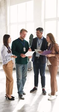 Business team wearing ID badges reviewing project documents, stand in office, engages in briefing before presentation or corporate training. Workshop attendance, professionals meeting, conference