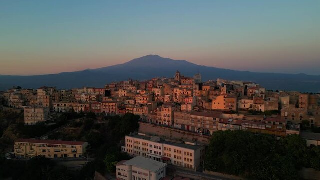 Aerial panorama of Centuripe at dusk with Mount Etna dominating the Sicilian landscape. Drone flyover of Centuripe highlighting dense historic buildings and dramatic volcanic scenery.