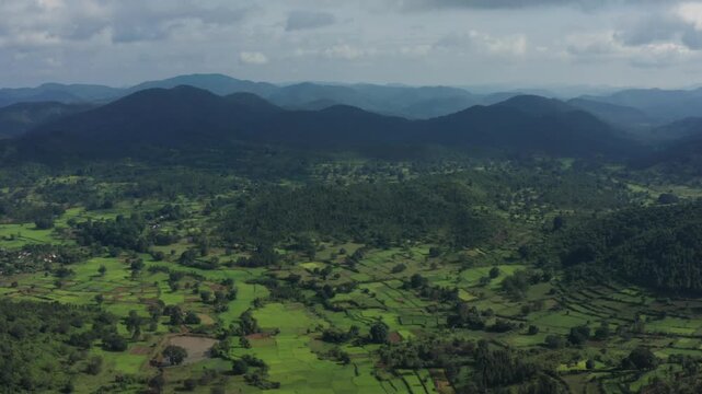 Sweeping aerial panorama of layered green hills with terraced paddy fields, scattered forests, and distant misty ridges around Daringbadi hill station in Odisha, India.