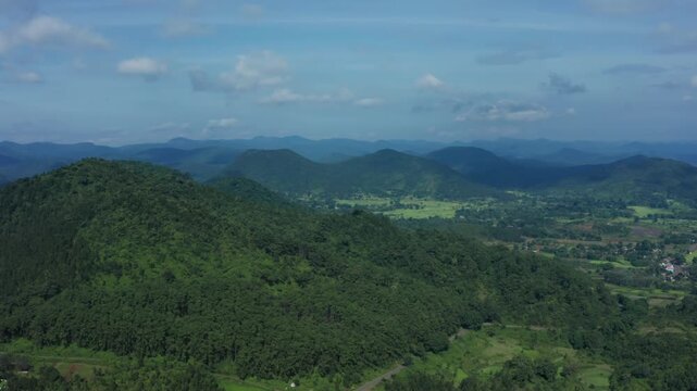 Expansive aerial of Daringbadi's layered green hills, deep valleys with scattered villages and fields under blue skies with scattered clouds.