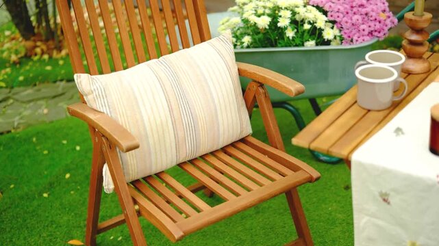 Wooden garden chair with striped cushion on green grass near flowers and mugs