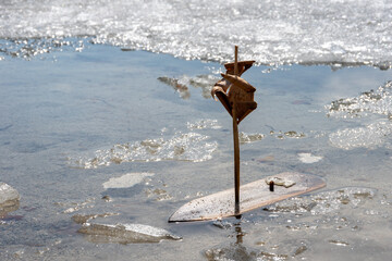 Small wooden sailboat model with a paper sail is anchored in shallow water surrounded by ice fragments. Spring outdoor games.