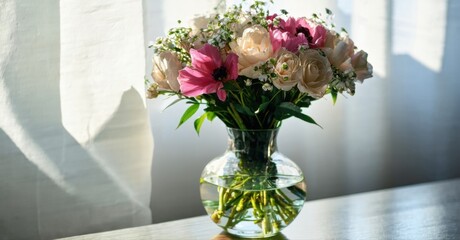 Floral arrangement sits upon surface. Soft light illuminates petals, stems, glass vase. Delicate beauty, peaceful scene.