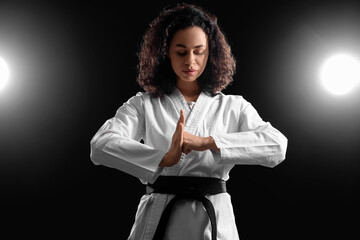 Young African-American woman practicing karate on dark background © Pixel-Shot