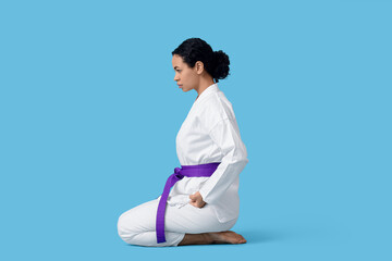 Young African-American woman practicing karate on blue background