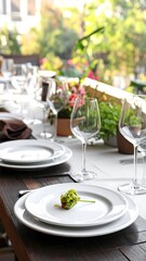 Fototapeta premium Outdoor table setting, white plates, wine glasses, flower centerpiece, sunny background
