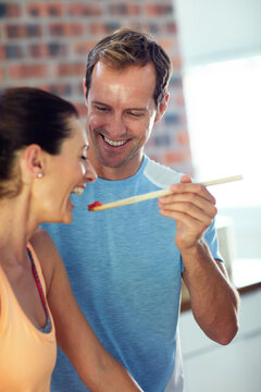 Happy couple, cooking and feed in kitchen with spoon, healthy meal and taste test for bonding together. Married people, smile and sample food in home for lunch preparation, fun and help with recipe.