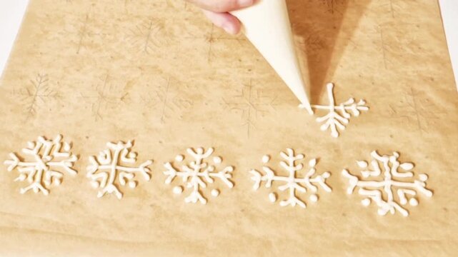 Hand piping white snowflake patterns with icing on parchment paper for baking