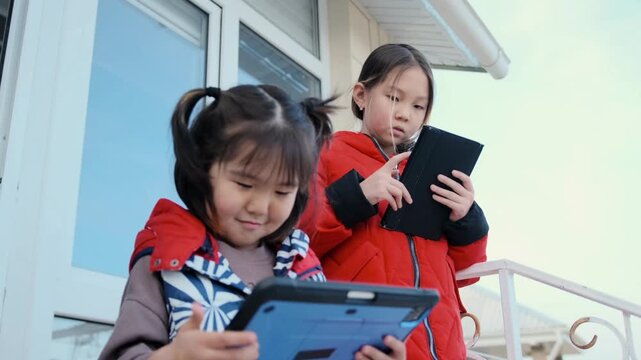 sisters sharing tablets, two young asian girls using tablet together, asian sisters with pigtails enjoying playful tablet time, closeup of asian sisters bonding over tablet in playful learning session