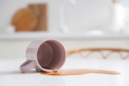 Overturned cup and spilled coffee on table in kitchen, closeup