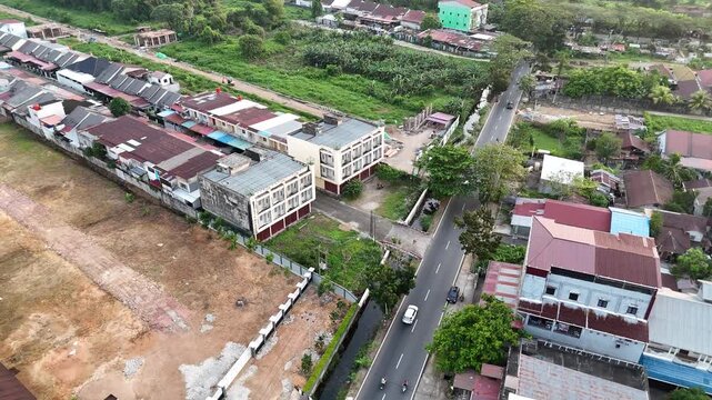 Aerial footage from a drone shows a suburban residential area with rows of closely packed houses and a main road with vehicles under a clear sky.