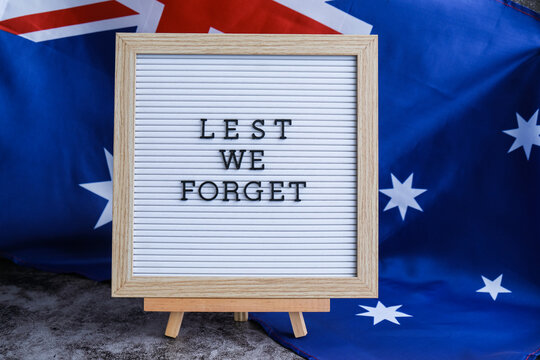 Somber Australian flag backdrop with text LEST WE FORGET on letter board. Respectful message for memorial ANZAC campaigns. Concept of remembrance and honor