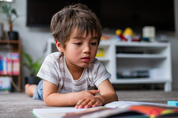 Young boy lying on his stomach, intently focused on a colourful book in a bright living room
