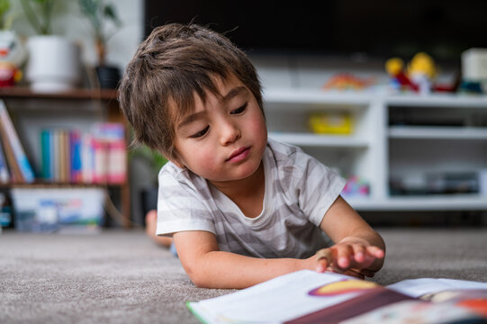 A little boy lies on his stomach, immersed in a book in a warm, inviting home environment