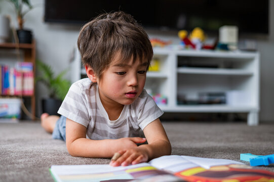 A child lies on his stomach, deeply engaged in reading a colourful book at home